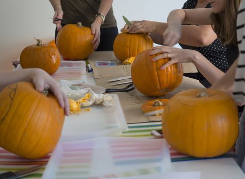 Group of people carving pumpkin to make Jack-o-lantern. Creating traditional decoration for Halloween and Thanksgiving. Cutted orange pumpkin lay on table