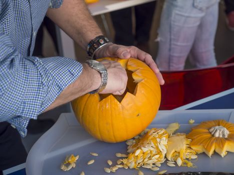 Process of carving pumpkin to make Jack-o-lantern. Creating traditional decoration for Halloween and Thanksgiving. Cutted orange pumpkin lay on table in man hands