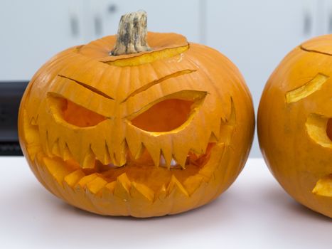 Halloween big orange pumpkin decorated with scary face. Jack O' Lantern on white table background.