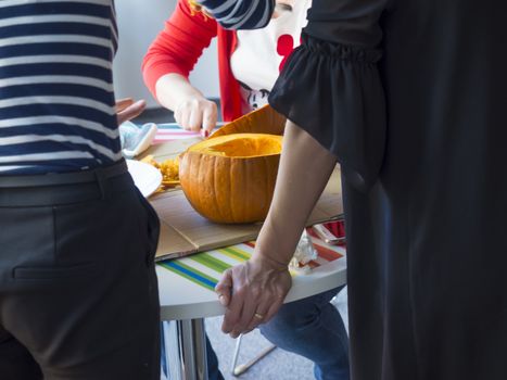 Group of people carving pumpkin to make Jack-o-lantern. Creating traditional decoration for Halloween and Thanksgiving. Cutted orange pumpkin lay on table