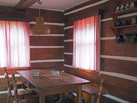 interior of old timbered cattage house with oak table chairs and painted cups with two windows with checked curtains