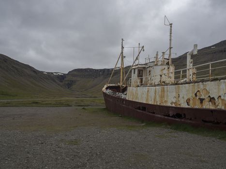 Old abandoned rusty fishing boat ship wreck standing on the sand beach coast in west fjords od Iceland, dramatic gray sky and hills background in Patreksfjordur, Iceland, west fjords,