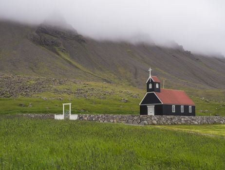 OLSaurbaejarkirkja black wooden red roof church on green grass field, steep hills in fog, Raudisandur, iceland west fjordsYMPUS DIGITAL CAMERA