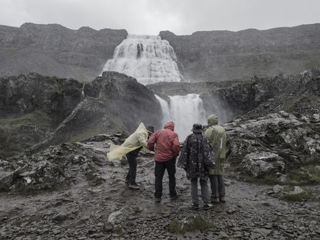 Group of tourist people in colorful raincoat watching Dynjandi waterfall, biggest in west fjords of Iceland, Vintage monochromatic look