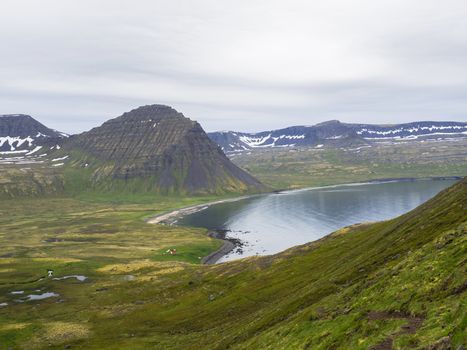 Northern summer landscape, View on beautiful snow covered cliffs and Alfsfell mountain, Hloduvik cove in Hornstrandir, west fjords, Iceland, with river stream, green meadow and abadoned farm budir, moody sky background