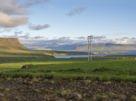 rural northern landscape with green grass and volcanic hills, aline pole, blue sky clouds, golden hour, summer in Iceland west fjords