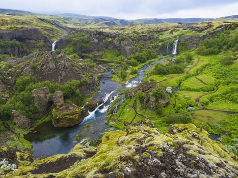 Beautiful Valley Gjain with colorful lava rocks, lush green moss and vegetation and blue water with waterfalls and cascade in south Iceland.