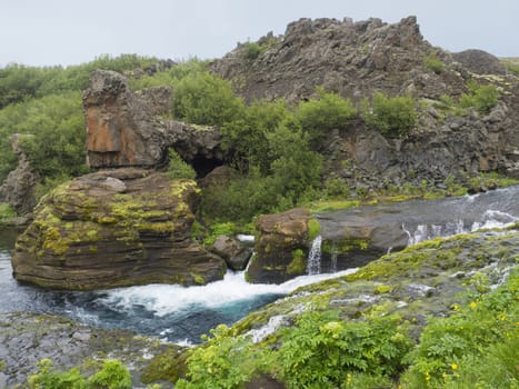 Beautiful Valley Gjain with colorful lava rocks, green vegetation and blue water stream cascade in south Iceland