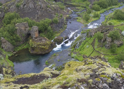 Beautiful Valley Gjain with colorful lava rocks, green vegetation and blue water stream cascade in south Iceland