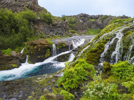 Beautiful Valley Gjain with colorful lava rocks, lush green moss and vegetation and blue water with waterfalls and cascade in south Iceland.