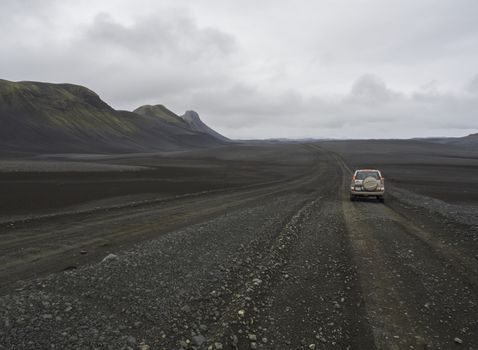 South Iceland, Nature reserve Fjallabak, July 4, 2018: Off road car Toyota Landcruiser driving on dirty mountain road through black lava sand desert landscape with green hills and moody sky