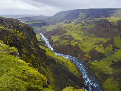 Landscape valley of river Fossa with blue water stream and green hills and moss covered cliffs, in South Iceland, summer moody sky.