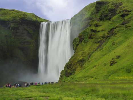 Beautiful Skogafoss waterfall in South Iceland Skogar with group of colorful dressed tourist people, long exposure motion blur, copy space