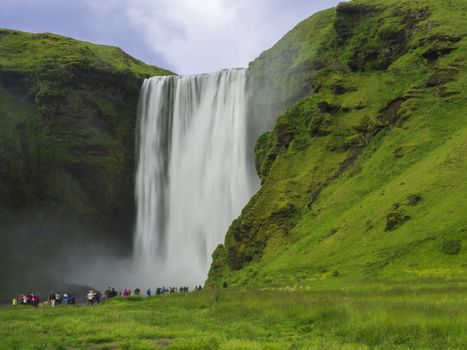 Beautiful Skogafoss waterfall in South Iceland Skogar with group of colorful dressed tourist people, long exposure motion blur, copy space