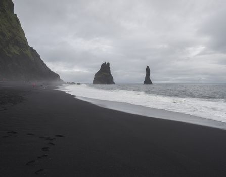 Basalt rock formations Troll toes on black sand beach reynisfjara with group of colorful tourist people, fog and moody sky, monochromatic look, Reynisdrangar, Vik, Iceland