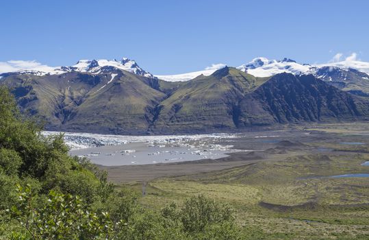 View on glacier lagoon with icebergs and tongue of Skaftafellsjokull, Vatnajokull spur and colorful snow covered rhyolit mountains in Skaftafell national park, Iceland