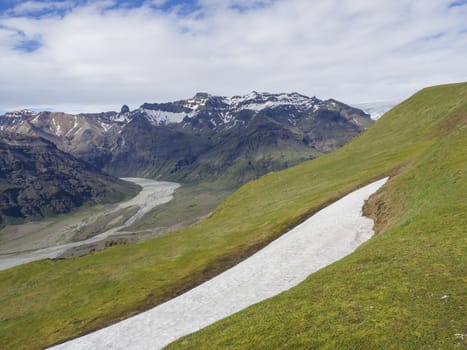 green grass slope and snow on green hill with view on glacier Skaftafellsjokull, and clorful rhyollite mountains, Skaftafell Park, South Iceland