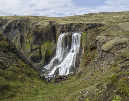 View on Beautiful Fragifoss waterfall on Geirlandsa river in South Iceland, green moss and rock, blue sky background