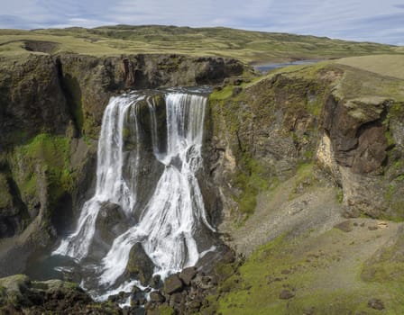 View on Beautiful Fragifoss waterfall on Geirlandsa river in South Iceland, green moss and rock, blue sky background