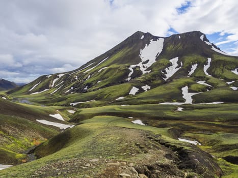 View on green moss and snow covered vulcanic mountain and creek stream in Maelifellssandi near road f210 in Iceland natue reserve Fjallabaki, white clouds blue sky