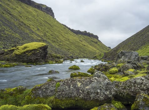 View on blue water stream and green moss covered stones and hills in Eldgja gorge in Iceland Fjallabak nature reserve, long exposure motion blur
