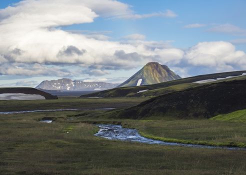 beatiful view from campsite Strutur on landscape with Maelifell mountain, green grass, blue water stream creek, snow patched hills, golden hour light and rainbow, nature reserve, Iceland