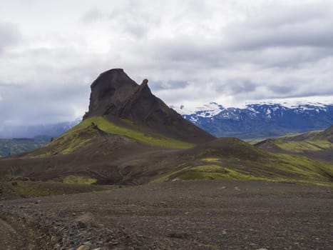 volcanic landscape in Nature reserve Fjallabak in central Iceland with mountain einhyrningur with green moss and blue snow covered mountain range, moody sky background