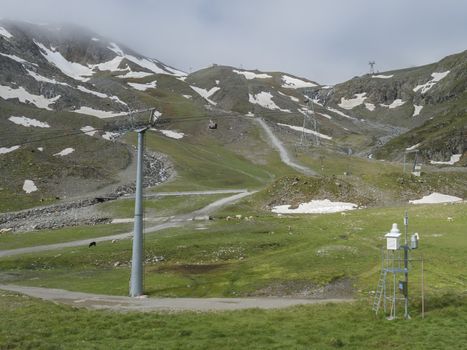 View on snow spotted mountain slopes at Mittelstation with Stubaier Gletscher gondola lift at Stubai Glacier in Tyrol, Austria and grazing sheep and cows, Summer.