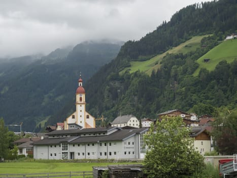 Summer morning foggy view on Neustift im Stubaital church at Stubaital or Stubai Valley near Innsbruck, Austria, green meadow and misty mountain peaks.