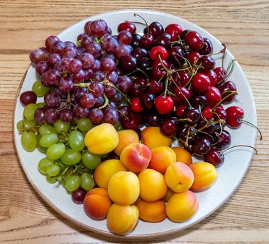 Fresh fruits on a plate. Fruit still life. Dish of fresh fruit. Grapes, cherries and peach on a plate. White utensils with fruits on a wooden surface