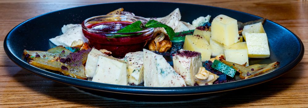 Farm cheeses. Three types of cheese and sauce on a black plate