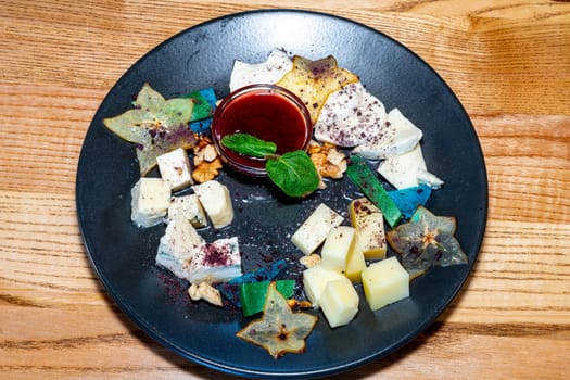 Farm cheeses. Three types of cheese and sauce on a black plate