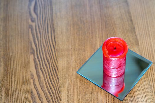 A thick red candle stands on the table. Side view. Place for text