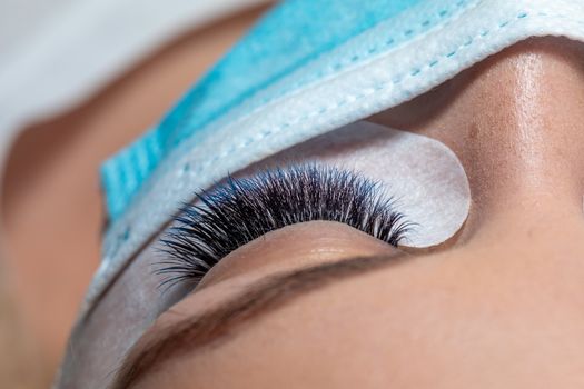 Treatment of Eyelash Extension in blue color Lashes. Eyes with Long Eyelashes and face with facemask