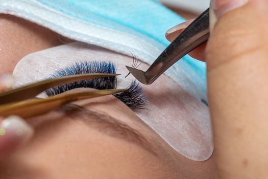 Treatment of Eyelash Extension in blue color Lashes. Eyes with Long Eyelashes and face with facemask