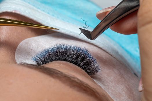 Treatment of Eyelash Extension in blue color Lashes. Eyes with Long Eyelashes and face with facemask