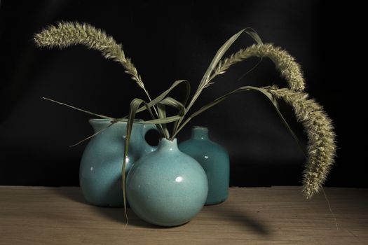 three blue vases still life on wooden table with wheat or corn it in on black background