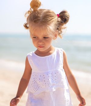 Little Caucasian girl 3 years old walks along the sea coast. Cute child portrait on the beach. Family vacation Summer season