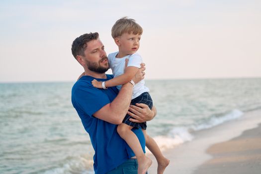 Father son spending time together sea vacation Young dad child little boy walking beach Fathers day. Family with one child. Happy childhood with daddy. sitting on hands laughs