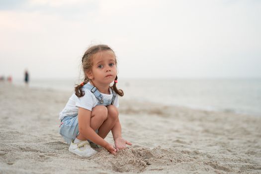 Child playing sand beach Little girl play sad alone summer family vacation Caucasian female 3 years old dressed denim near sea water