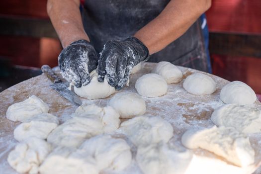 Chef in black gloves cuts raw dough into pieces make pizza Patties bread. Street food process. Bakary culinary.