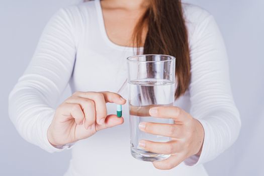 Close up Asian woman holding a glass of water and pill drugs in hand on grey background. Healthcare and medical pharmacy concept