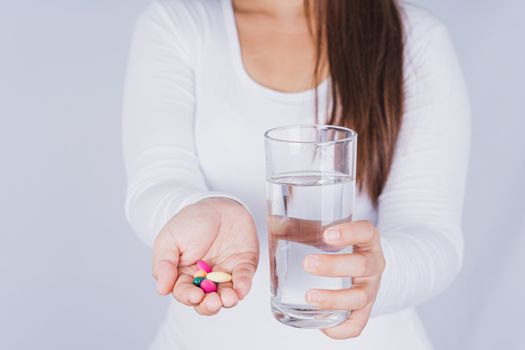 Close up Asian woman holding a glass of water and pill drugs in hand on grey background. Healthcare and medical pharmacy concept