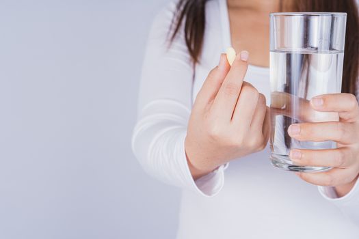 Close up Asian woman holding a glass of water and pill drugs in hand on grey background. Healthcare and medical pharmacy concept