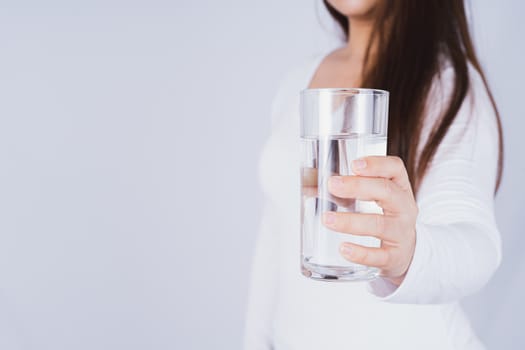 Close up Asian woman holding a glass of water in hand on grey background. Healthcare and medical pharmacy concept