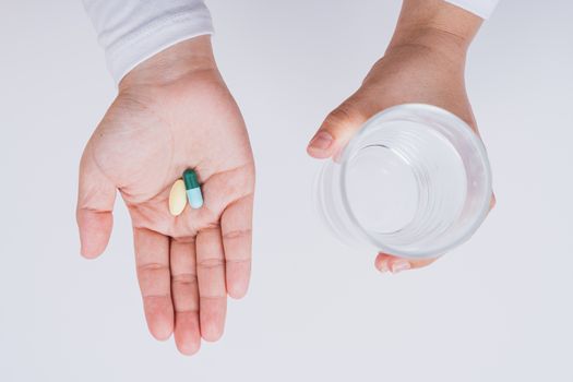 Close up Asian woman holding a glass of water and pill drugs in hand on grey background. Healthcare and medical pharmacy concept