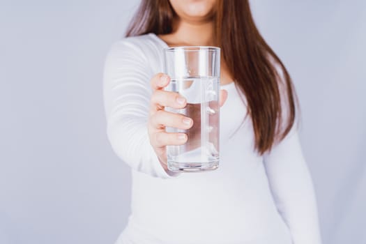 Close up Asian woman holding a glass of water in hand on grey background. Healthcare and medical pharmacy concept