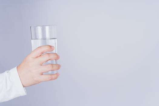 Close up Asian woman holding a glass of water in hand on grey background. Healthcare and medical pharmacy concept