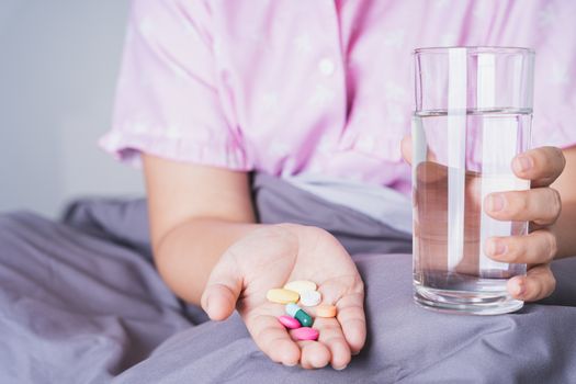 Close up female patient holding a glass of water and pill drugs in the bedroom. Healthcare and medical pharmacy concept