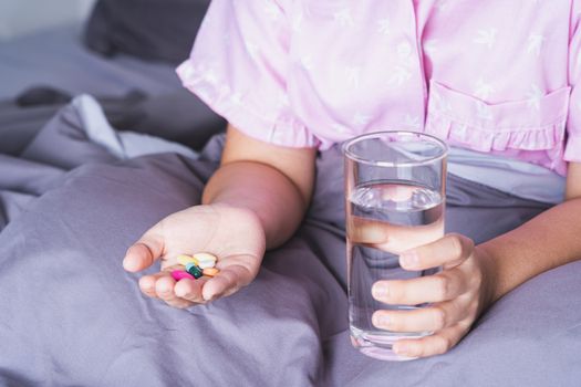 Close up female patient holding a glass of water and pill drugs in the bedroom. Healthcare and medical pharmacy concept